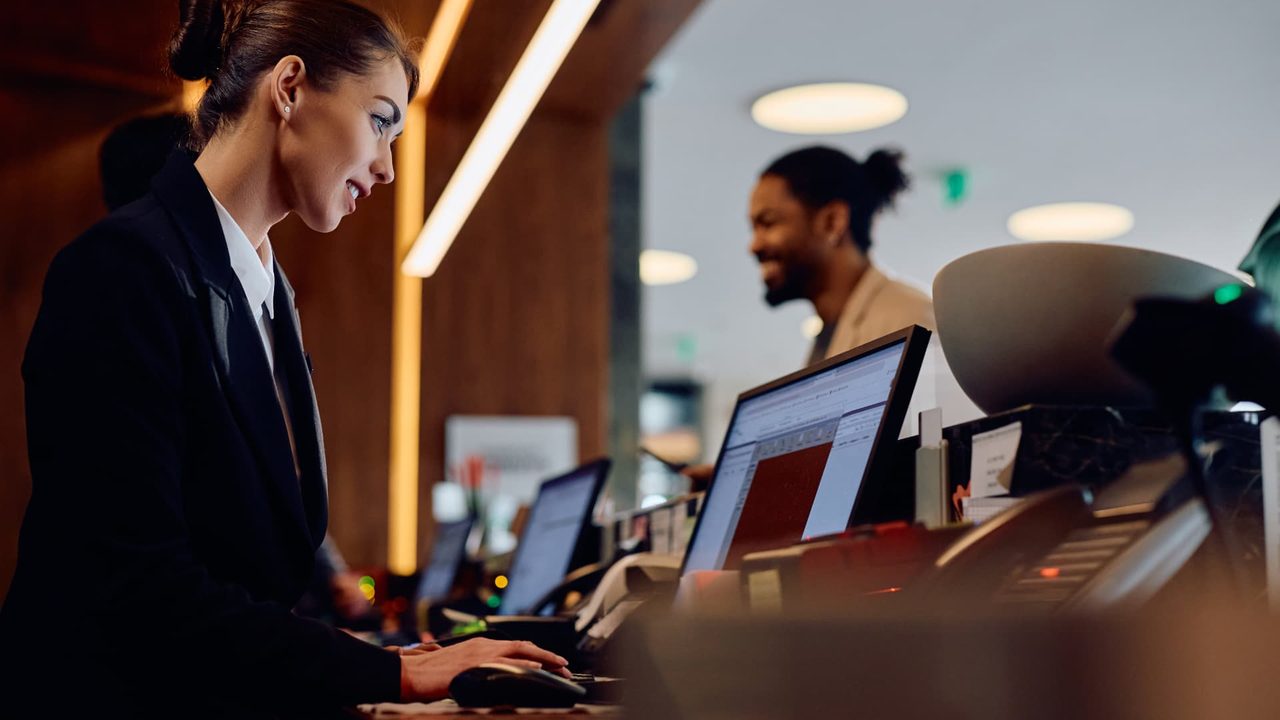 Hotel front desk team working at reception workstations, using connected property systems to serve arriving guests.