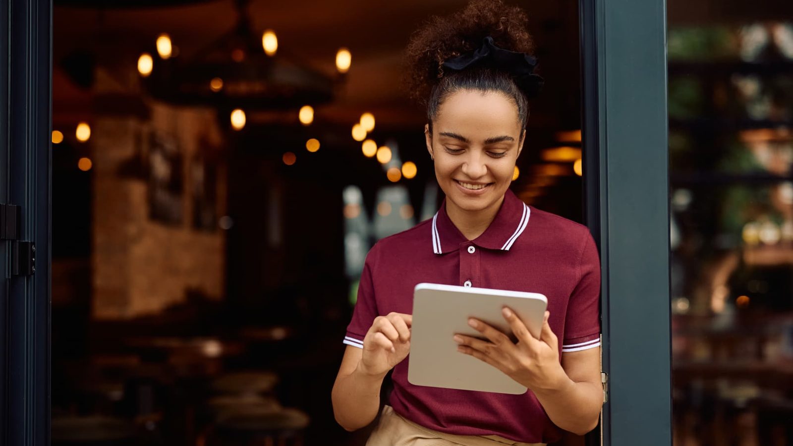 A waitress smiling while using a tablet in the doorway of a restaurant