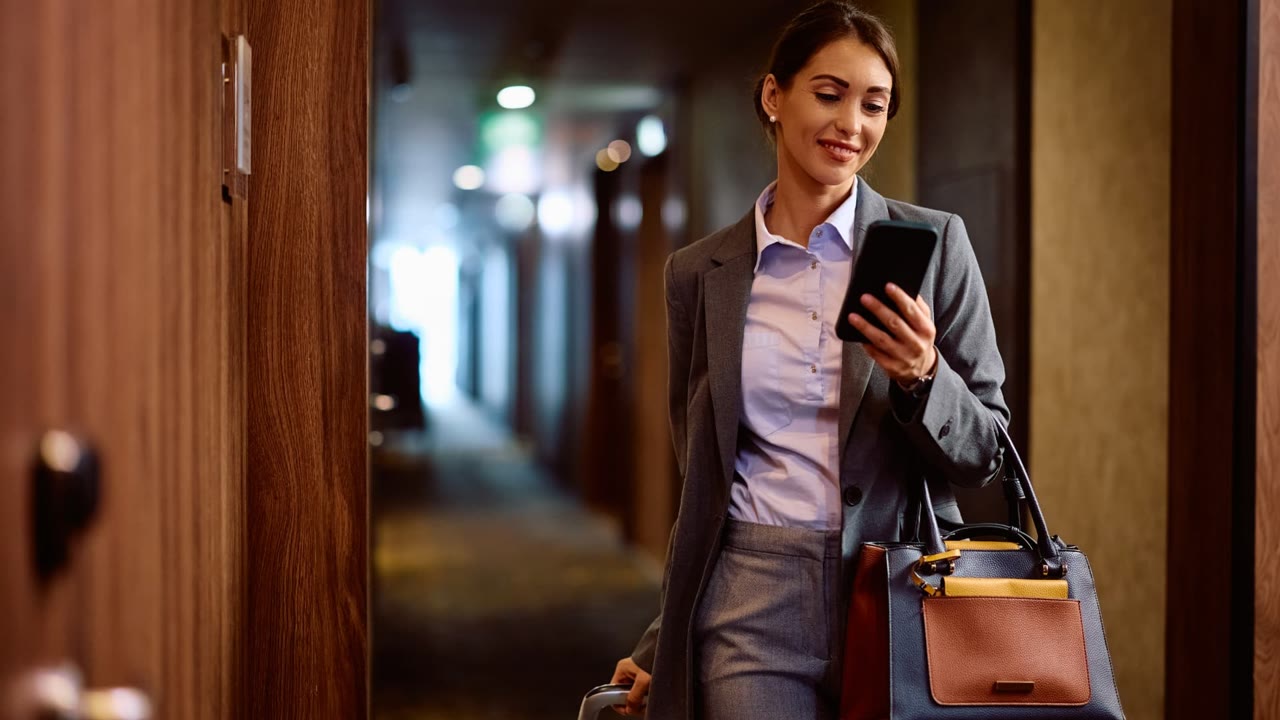 Hotel guest checking her phone in a hotel corridor while arriving with her luggage